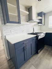 Kitchen with glass fronted cabinets, blue cabinetry, dark wood-style floors, stainless steel gas range oven, and light stone countertops