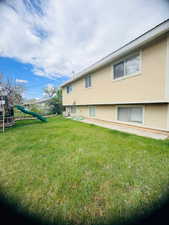 Rear view of house with stucco siding, a lawn, and a playground