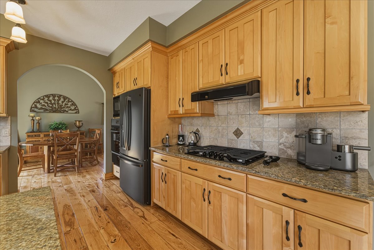 Kitchen with backsplash, fridge with ice dispenser, dark stone counters, light wood-type flooring, and vaulted ceiling