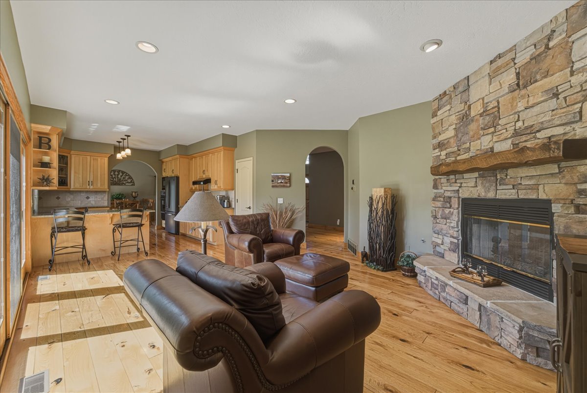Living room featuring arched walkways, a stone fireplace, light wood finished floors, and recessed lighting