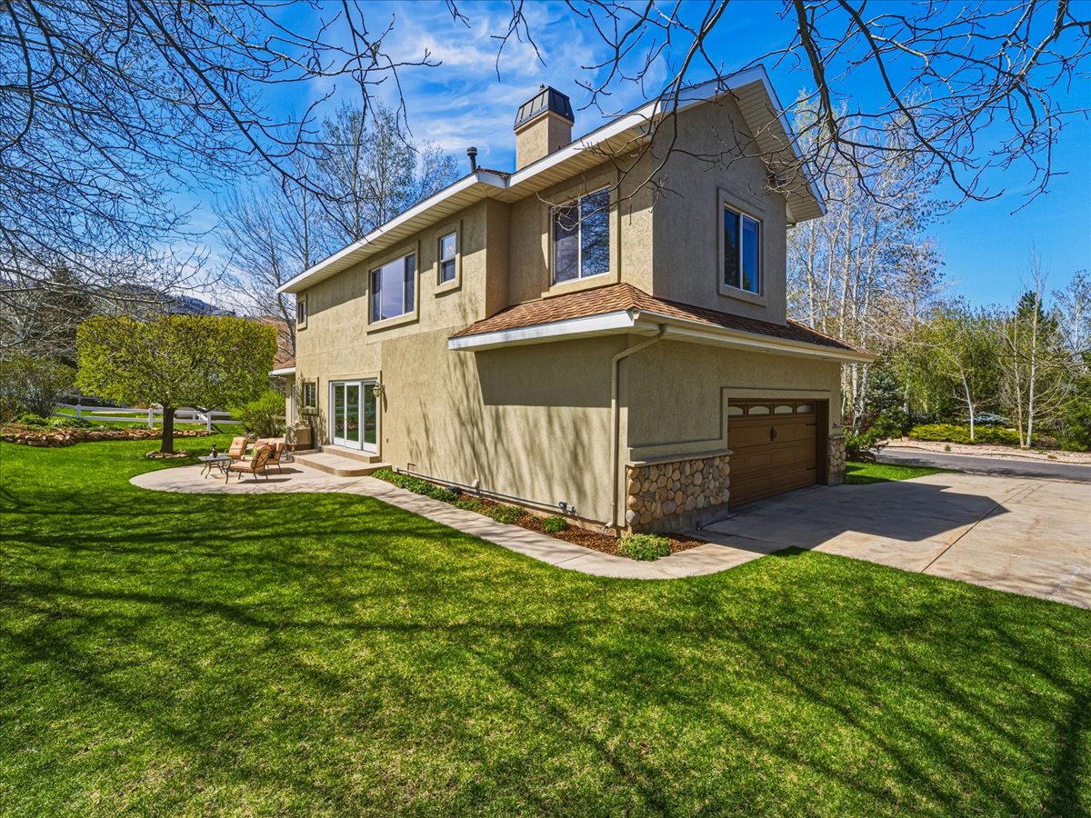 View of side of property with stucco siding, concrete driveway, a garage, a chimney, and a yard