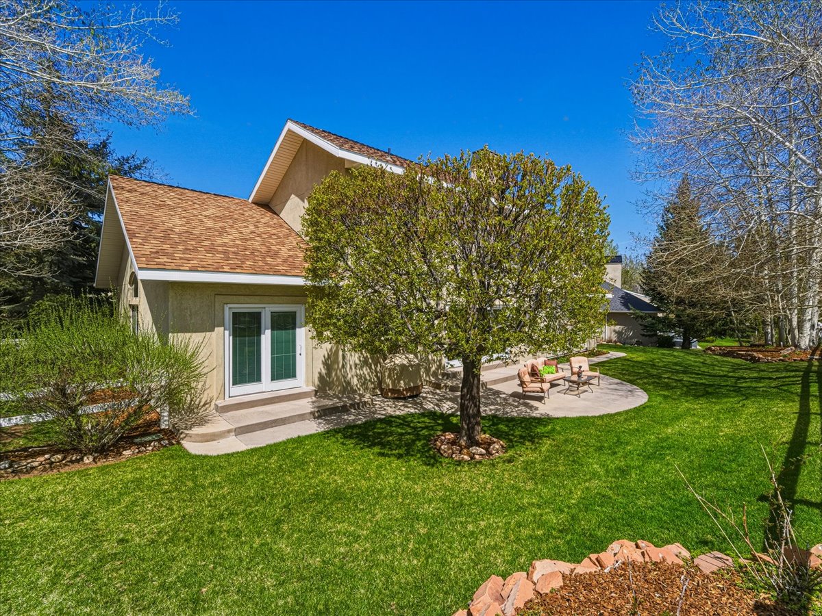 Rear view of property with a yard, a shingled roof, stucco siding, and a patio