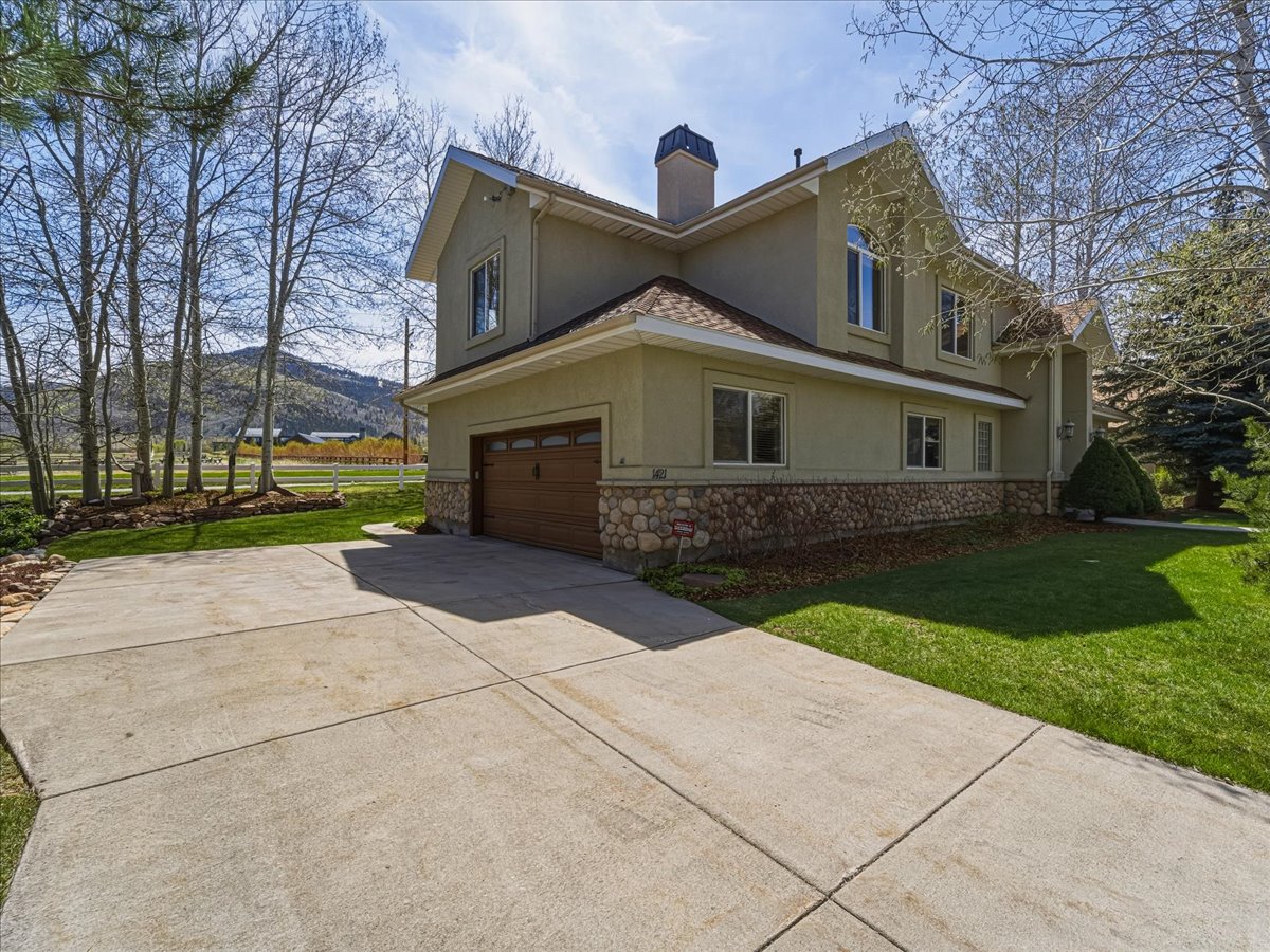 View of side of property featuring stucco siding, stone siding, a lawn, and a chimney