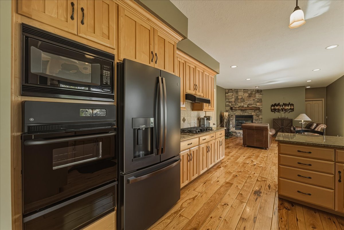 Kitchen featuring a fireplace, black appliances, a warming drawer, light wood finished floors, and open floor plan