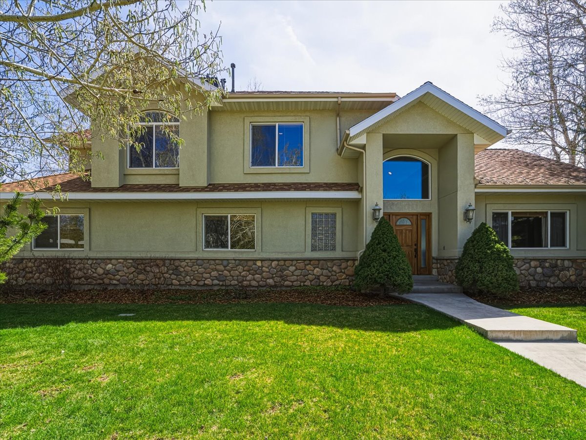 View of front of property featuring stone siding, stucco siding, a front yard, and a shingled roof