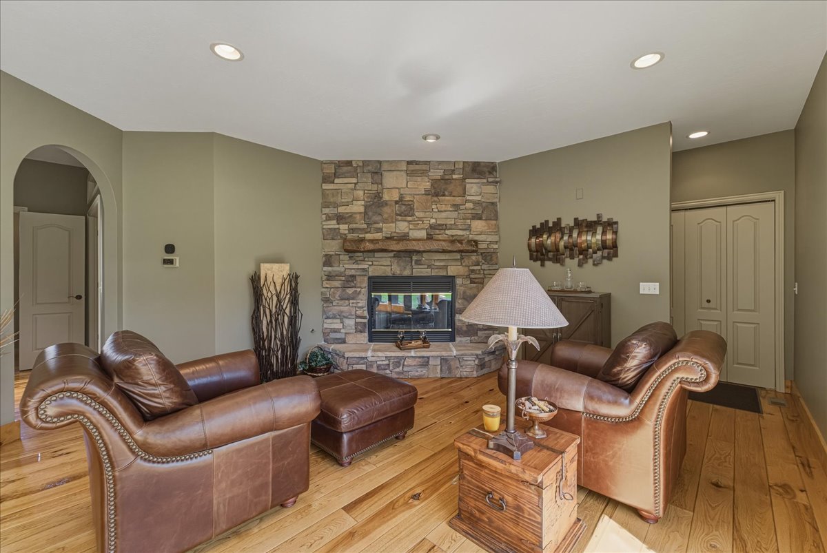 Living room with a stone fireplace, light wood finished floors, arched walkways, and recessed lighting