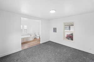 Unfurnished bedroom with light carpet, ensuite bathroom, and electric panel