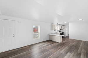 Unfurnished living room featuring dark wood-style floors, healthy amount of natural light, and lofted ceiling