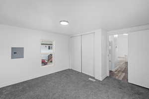 Unfurnished bedroom with dark colored carpet, electric panel, and a closet