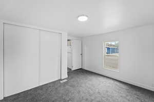 Unfurnished bedroom with a closet, dark carpet, and freestanding refrigerator