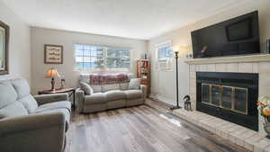 Living room featuring wood finished floors, cooling unit, a tile fireplace, and a textured ceiling