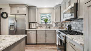 Kitchen featuring stainless steel appliances, light stone counters, light wood-style floors, a textured ceiling, and decorative backsplash