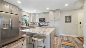 Kitchen featuring stainless steel appliances, light stone countertops, a kitchen island, a breakfast bar, and light wood finished floors