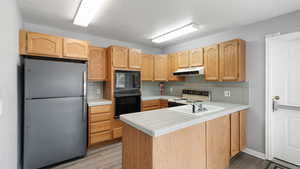Kitchen with tile counters, black appliances, a peninsula, backsplash, and light wood-type flooring