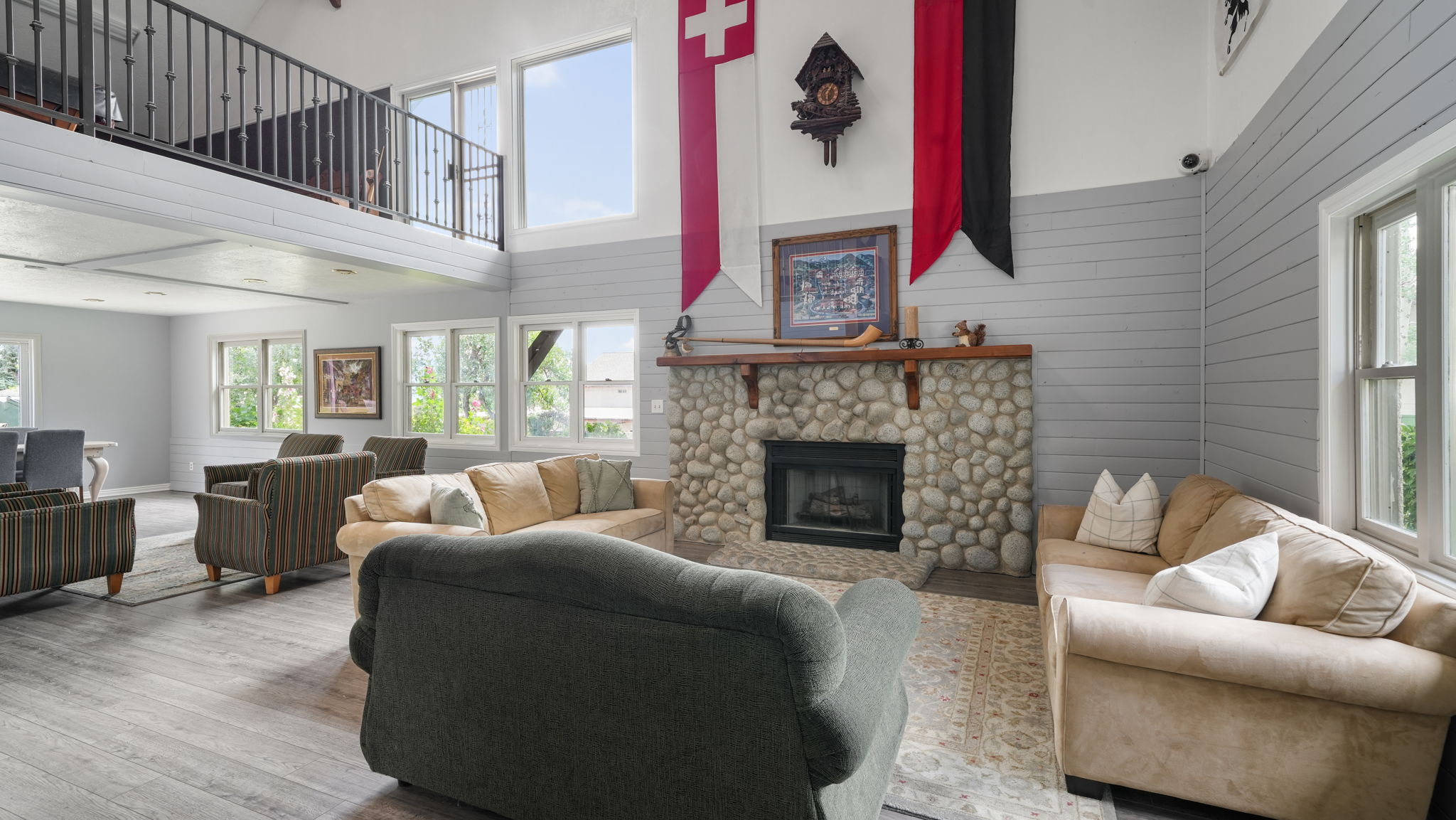 Living area with hardwood / wood-style floors, a stone fireplace, wooden walls, healthy amount of natural light, and a high ceiling