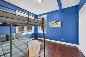 Bedroom with dark wood finished floors, beamed ceiling, and a textured ceiling