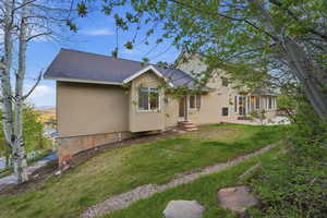 Rear view of house with roof with shingles, a lawn, stucco siding, and a patio
