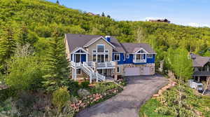 View of front of home with an attached garage, driveway, stone siding, a chimney, and a shingled roof
