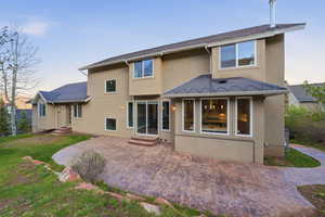 Back of house at dusk with stucco siding, a patio area, entry steps, and a yard