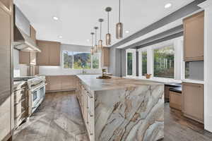 Kitchen with light wood finish cabinetry, a center island, light stone counters, and range with two ovens