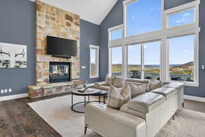 Living room with a stone fireplace, hardwood / wood-style flooring, and vaulted ceiling