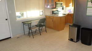 Kitchen Dining area with light countertops, glass fronted cabinets, stainless steel microwave, electric range, and wood finish cabinets