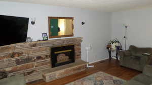 Living area featuring dark wood-type flooring, a stone fireplace, and a textured ceiling