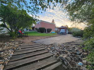 Inviting outdoor area featuring a wooden walkway, stone landscaping, mature trees, and a paved path leading to the gazebo