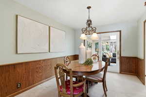 Dining space with wooden walls, wainscoting, light colored carpet, and suspended lighting