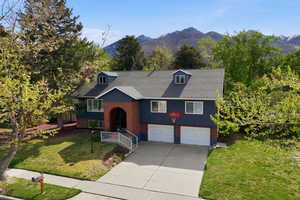 Split foyer home with a front lawn, an attached garage, driveway, a shingled roof, and a mountain view