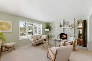 Living room with a fireplace, light colored carpet, and plantation shutters.