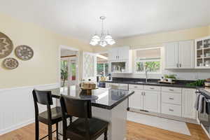 Kitchen with white cabinetry, a breakfast bar, light wood finished floors, wainscoting, and glass fronted cabinets