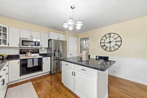 Kitchen featuring stainless steel appliances, white cabinets, light wood-type flooring, a kitchen island, and dark stone countertops