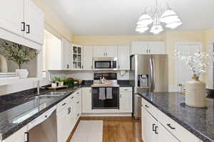 Kitchen with stainless steel appliances, dark stone countertops, white cabinetry, and glass fronted cabinets