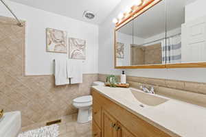 Main bathroom with vanity, tile walls, wainscoting, and light tile patterned floors