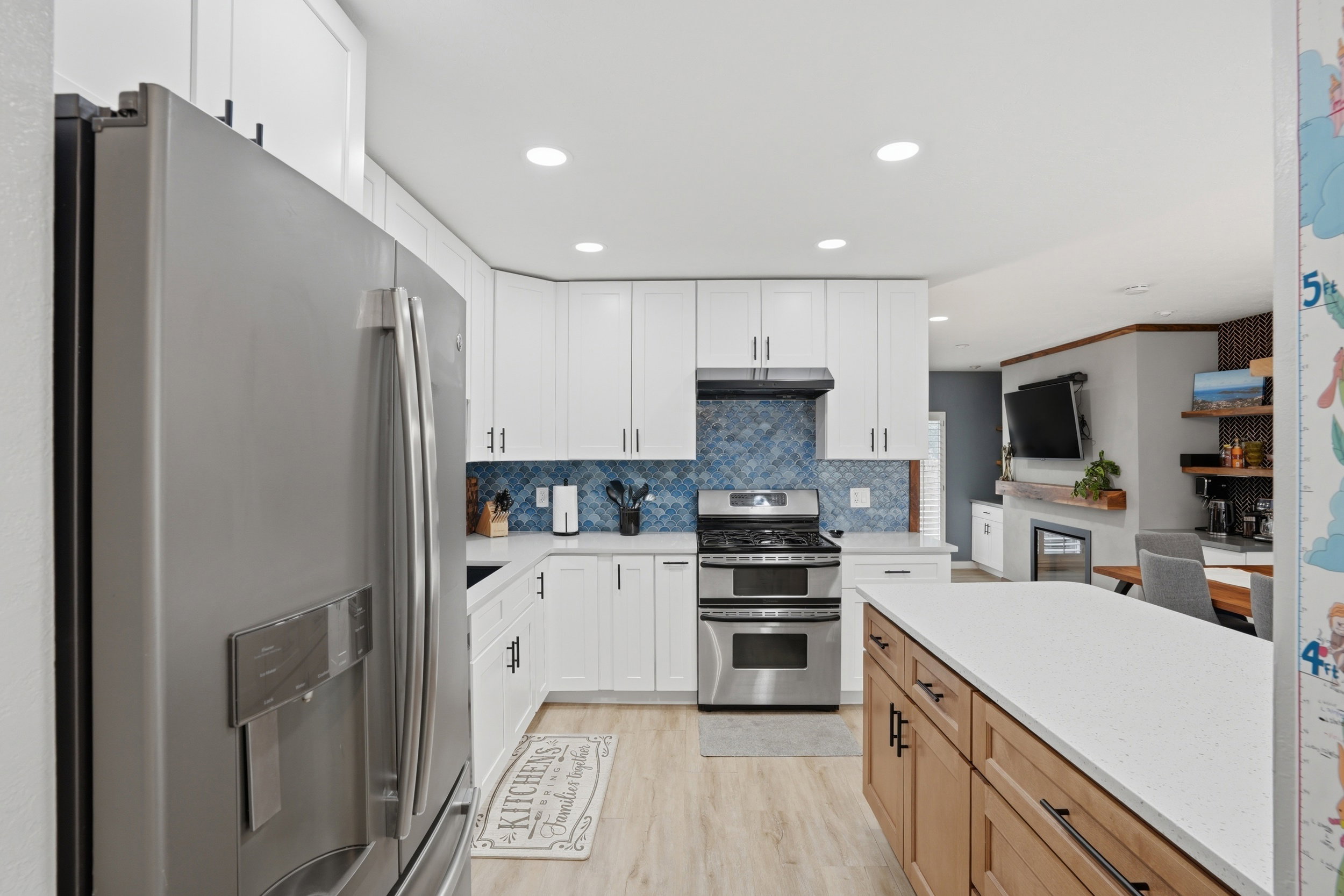 Two tone kitchen with stainless steel appliances, two tone color scheme, light wood finished floors, light stone counters, and recessed lighting