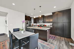 Kitchen with a kitchen island with sink, light wood-style floors, light countertops, stainless steel appliances, and decorative light fixtures