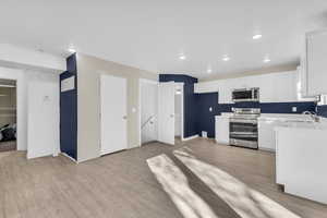 Kitchen with stainless steel appliances, white cabinetry, light wood finished floors, and recessed lighting