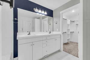 Bathroom featuring double vanity, light carpet, light marble finish flooring, and a walk in closet
