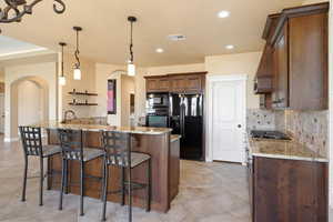 Kitchen featuring light stone countertops, a kitchen breakfast bar, black appliances, and arched walkways