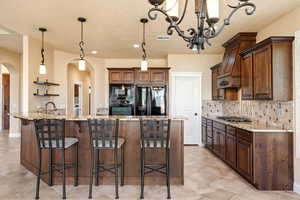 Kitchen with light stone counters, a breakfast bar, arched walkways, black appliances, and decorative light fixtures