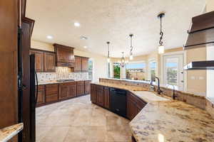 Kitchen featuring a chandelier, black appliances, dark wood finish cabinetry, backsplash, and light stone countertops