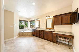 Full bath with double vanity, a textured ceiling, a garden tub, and recessed lighting