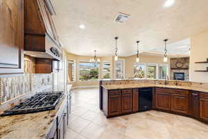 Kitchen with dark wood finish cabinetry, light stone countertops, open floor plan, black appliances, and a textured ceiling