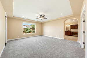 Unfurnished room with a tray ceiling, arched walkways, recessed lighting, light carpet, and a ceiling fan