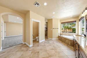 Bathroom with a garden tub, a textured ceiling, tiled shower, vanity, and recessed lighting