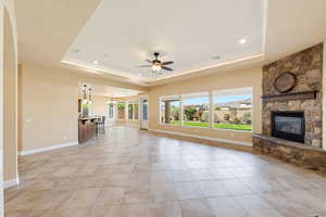 Unfurnished living room featuring ceiling fan, a fireplace, a raised ceiling, light tile patterned floors, and suspended lighting