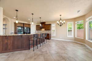 Kitchen featuring a kitchen bar, light stone counters, suspended lighting, decorative backsplash, and black appliances