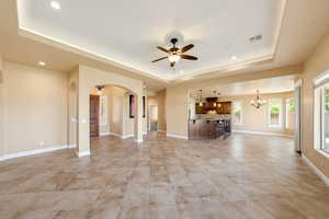 Unfurnished living room with a ceiling fan, a tray ceiling, hanging lights, and arched walkways