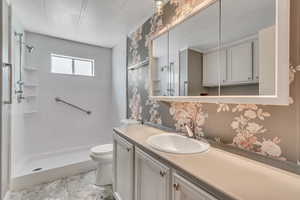 Full bath with wallpapered walls, vanity, and a walk in shower